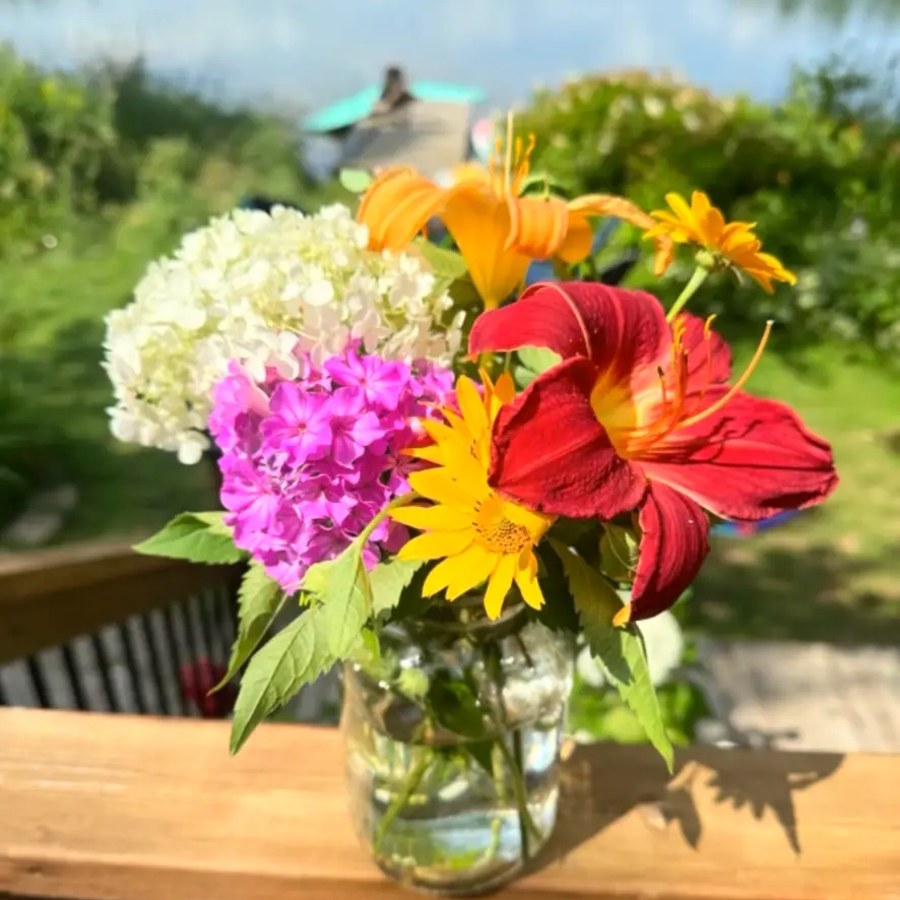 Mason jar of wildflowers on a deck railing overlooking the lake