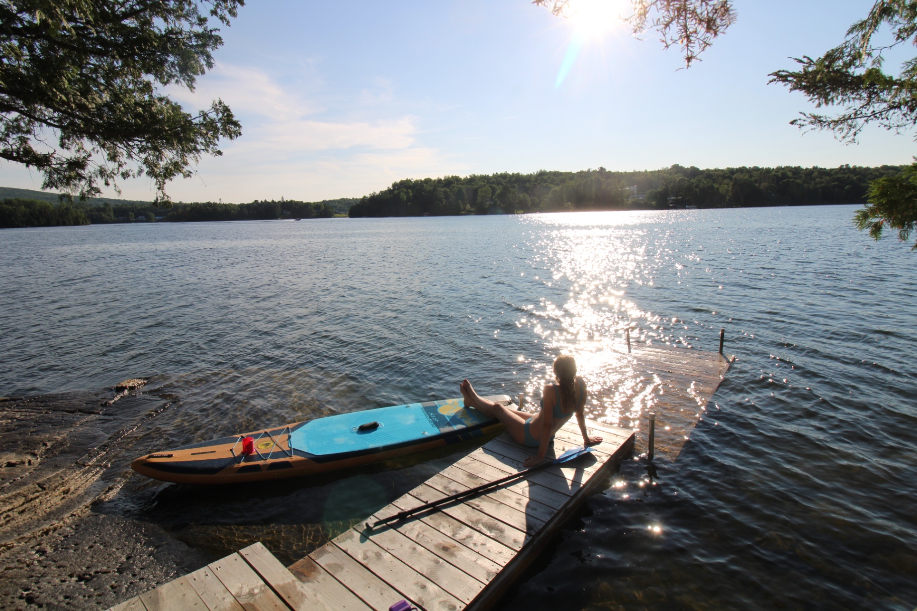 Sunlit lake view with a paddleboard resting on a wooden dock